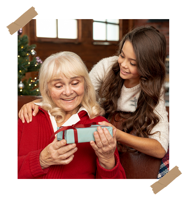 A young woman gifting a present to her smiling grandmother in a cozy holiday setting, symbolizing the joy of giving a LifeStory keepsake book.