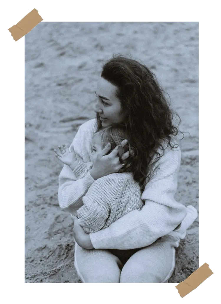 A black and white image of a mother embracing her child on the beach, capturing a tender moment of love and warmth.